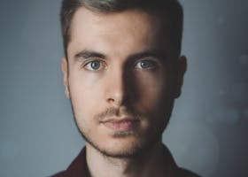 Close-up portrait of a young man with facial hair and a serious expression.