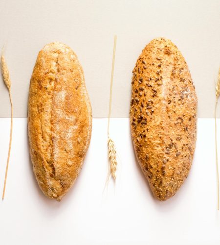 Flat lay image of two artisan bread loaves with wheat decoration on a neutral background.